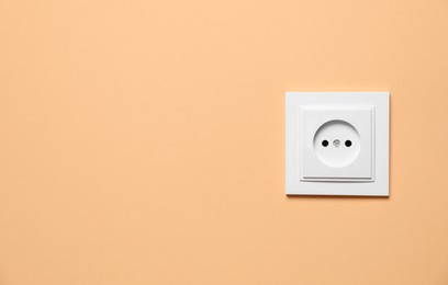 Photo of Power socket on pale orange wall, space for text. Electrical supply