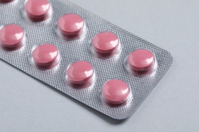 Photo of Pink pills in blister on grey background, closeup
