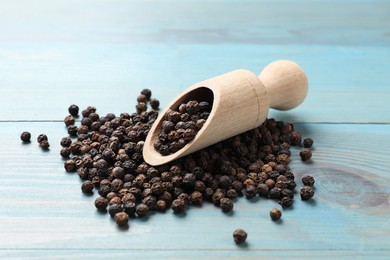 Photo of Aromatic spice. Black pepper in scoop on light blue wooden table, closeup