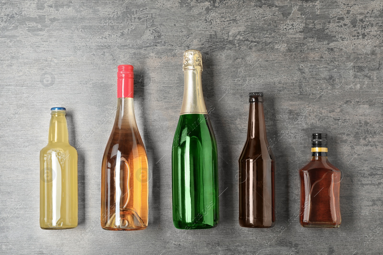 Photo of Bottles with different alcoholic drinks on grey background, top view