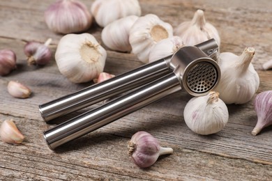 Garlic press and bulbs on wooden table, closeup