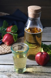 Photo of Delicious cider, red apples and green leaves on wooden table, closeup