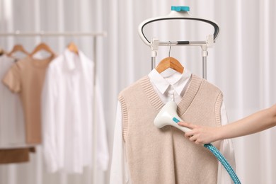 Woman steaming clothes on hanger at home, closeup. Space for text