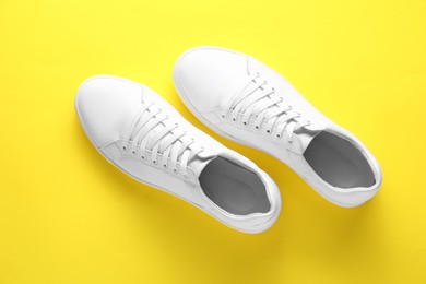 Photo of Pair of stylish white sneakers on yellow background, top view