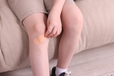 Photo of Little boy putting sticking plaster onto knee on sofa, closeup