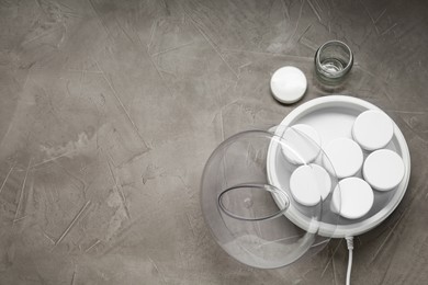 Photo of Modern yogurt maker with jars on grey table, flat lay. Space for text