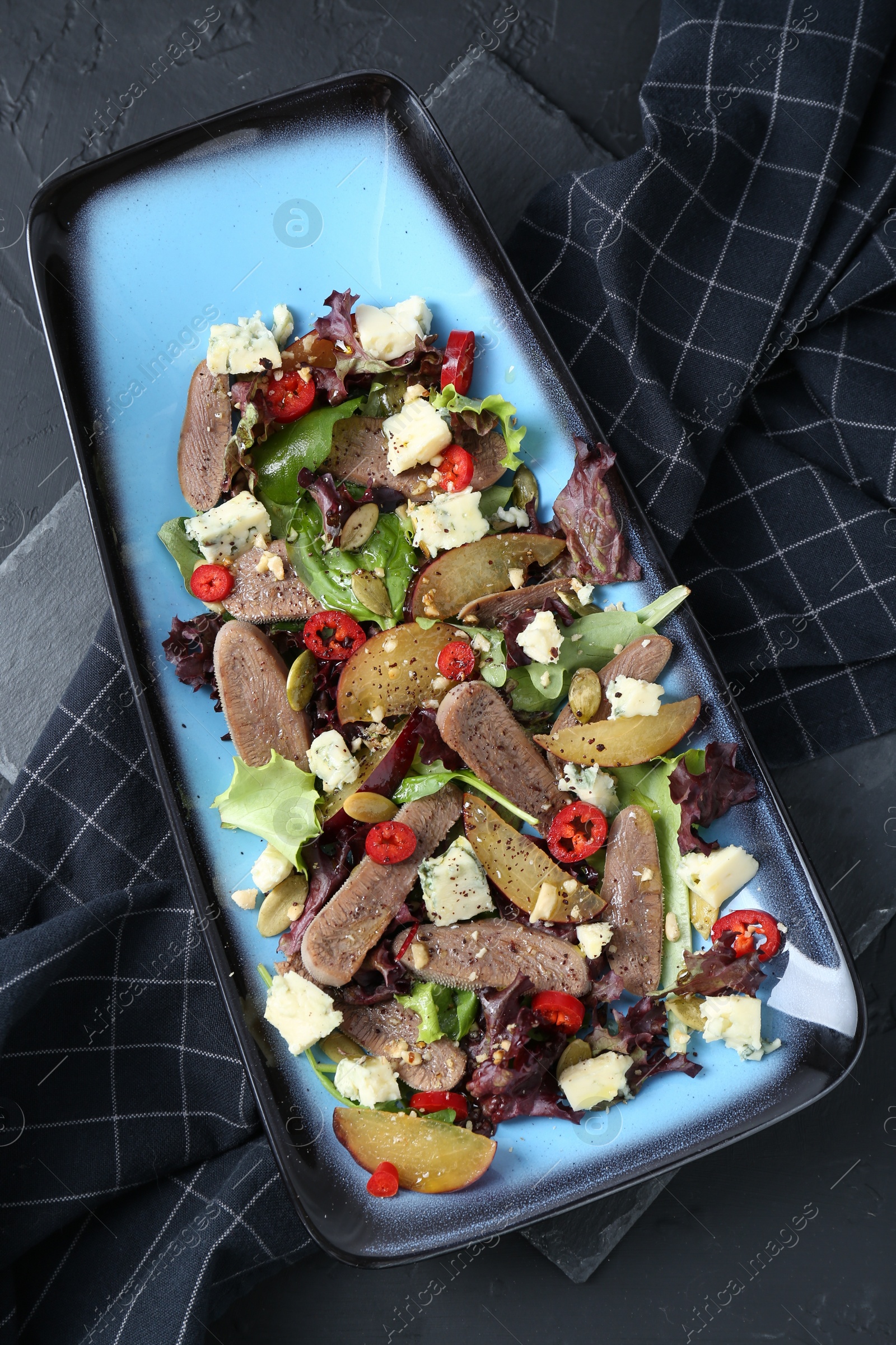 Photo of Delicious salad with beef tongue and cheese on black textured table, top view