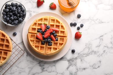 Tasty Belgian waffles with fresh berries and honey on white marble table, flat lay