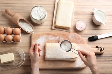 Photo of Young woman with puff pastry dough and ingredients on wooden table, top view