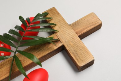 Wooden cross, painted Easter eggs and palm leaf on light grey background