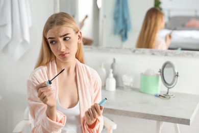 Young woman holding mascara brush with fallen eyelashes indoors