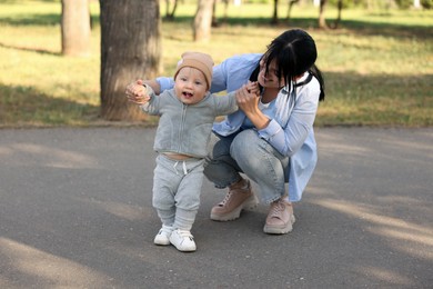 Photo of Mother supporting her baby while he learning to walk outdoors