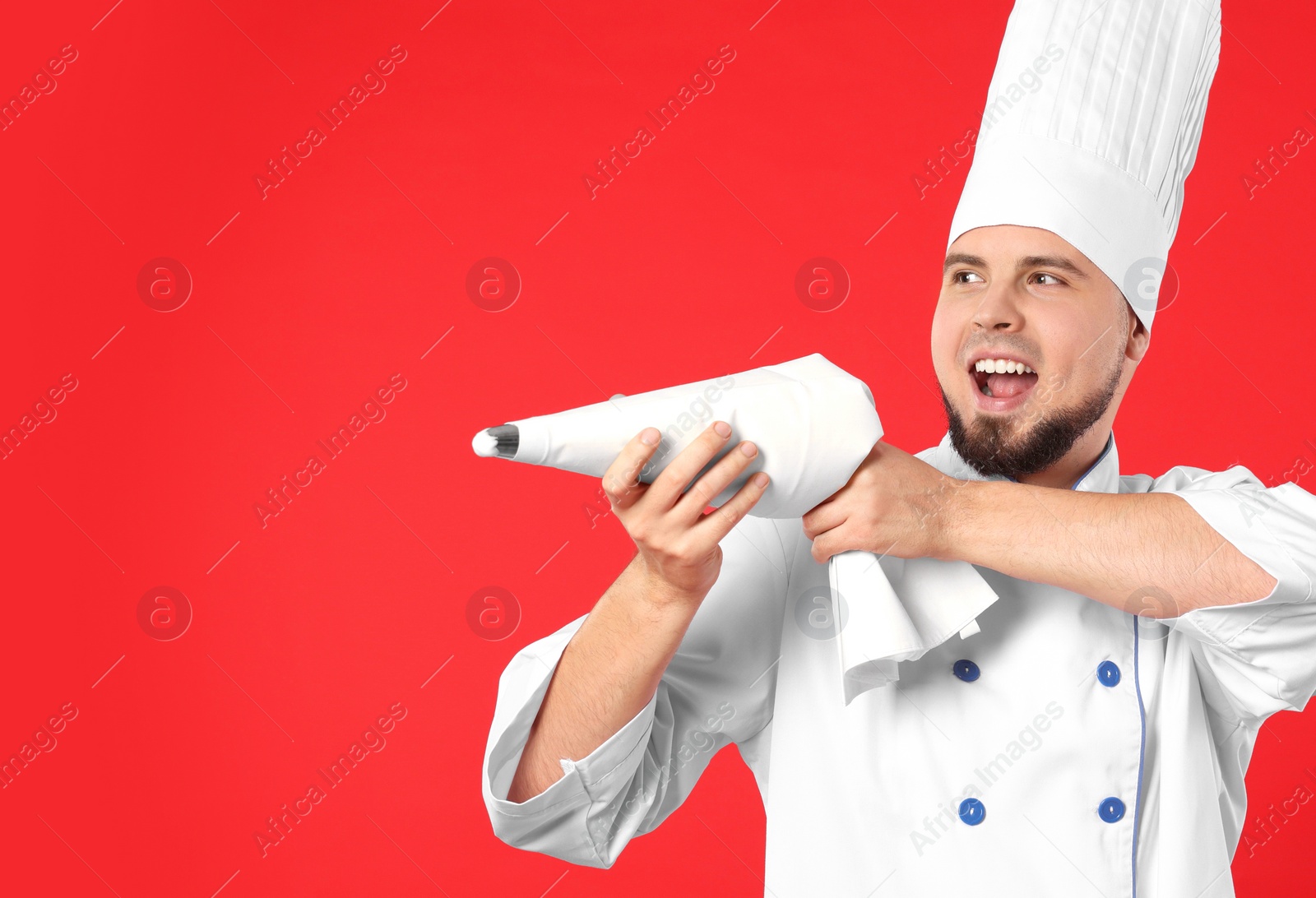 Photo of Happy professional confectioner in uniform having fun with piping bag on red background. Space for text