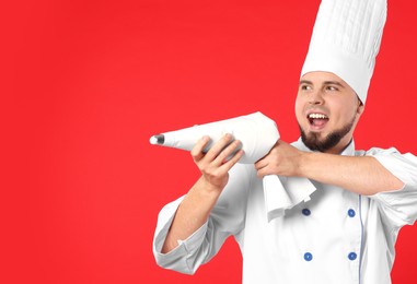 Happy professional confectioner in uniform having fun with piping bag on red background. Space for text