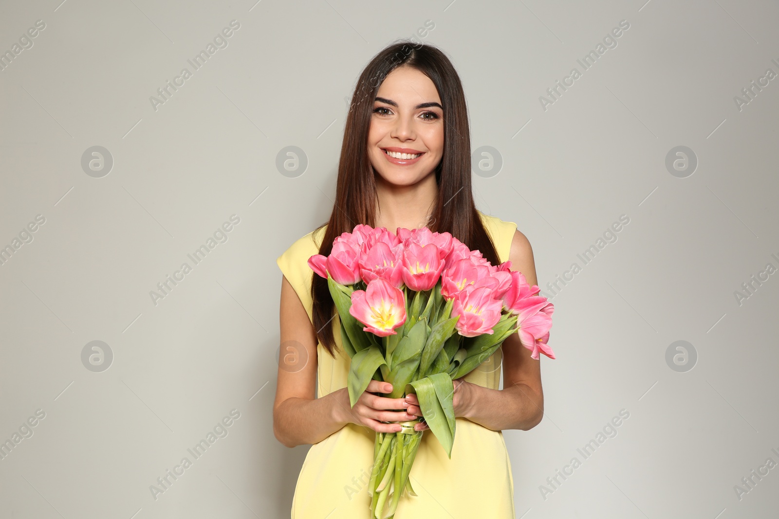 Photo of Portrait of beautiful smiling girl with spring tulips on light background. International Women's Day