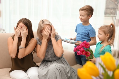 Photo of Cute little children congratulating mother and grandmother at home