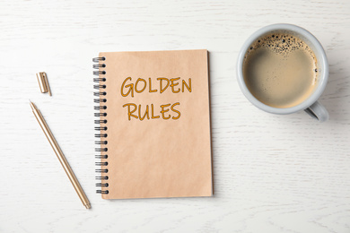 Image of Notebook with phrase GOLDEN RULES and cup of coffee on wooden background, top view