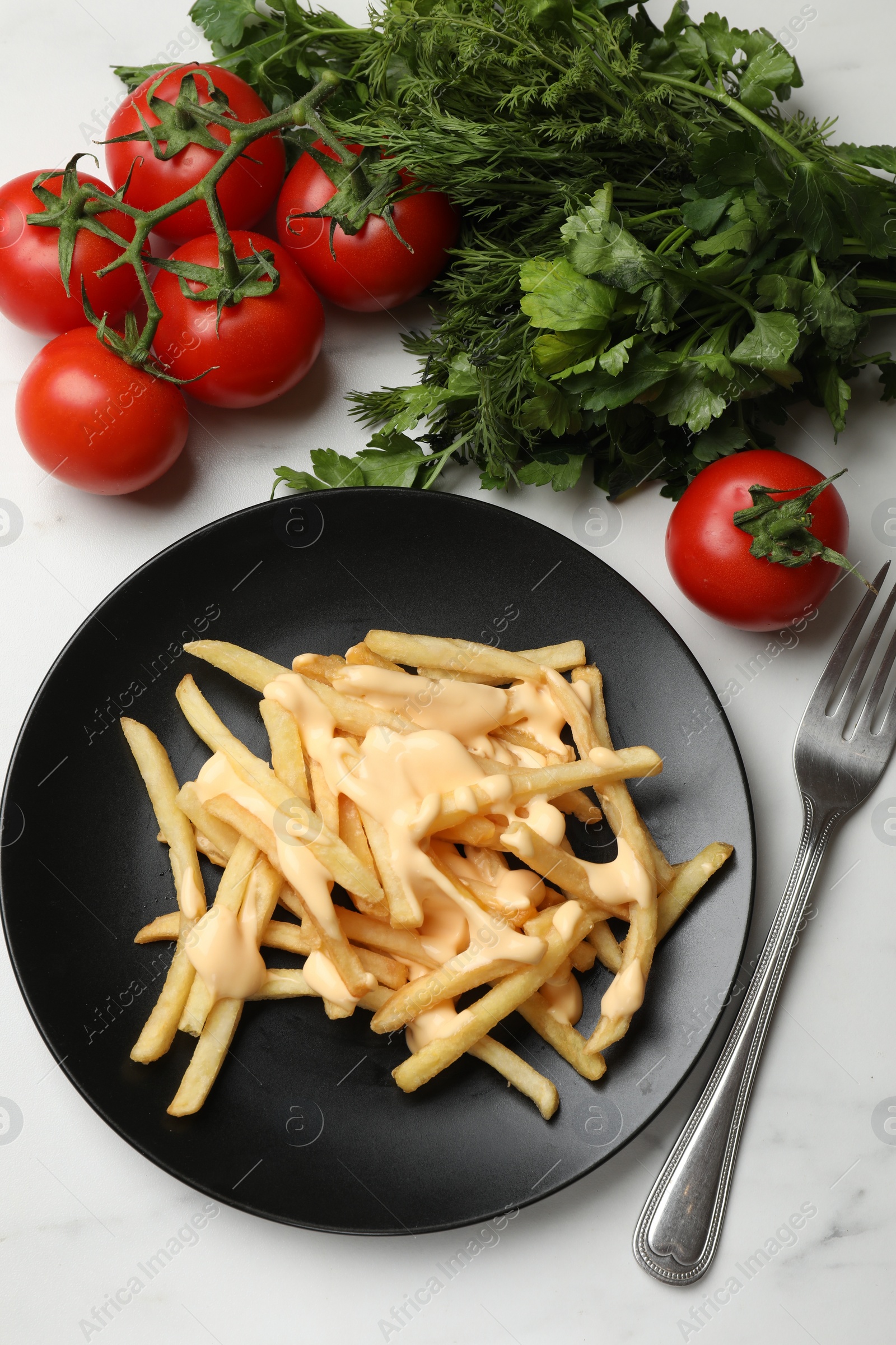 Photo of Delicious French fries with cheese sauce, tomatoes, dill and parsley on white marble table, flat lay