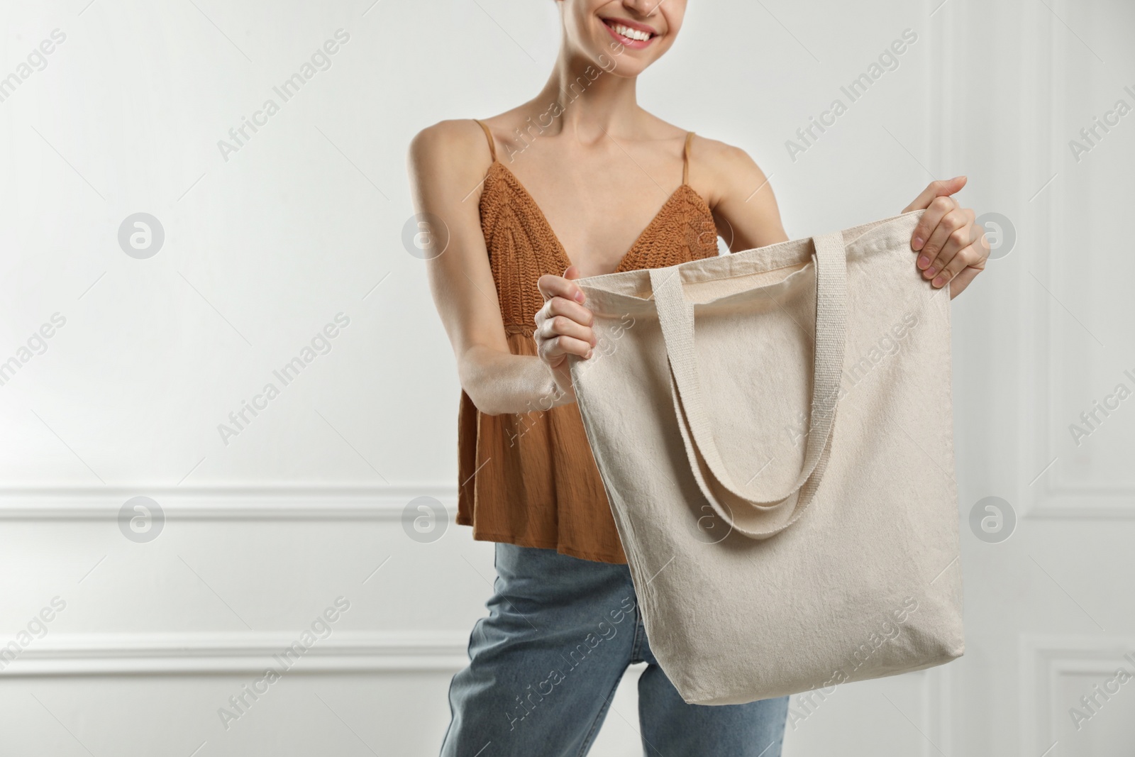 Photo of Happy young woman with blank eco friendly bag near white wall, closeup