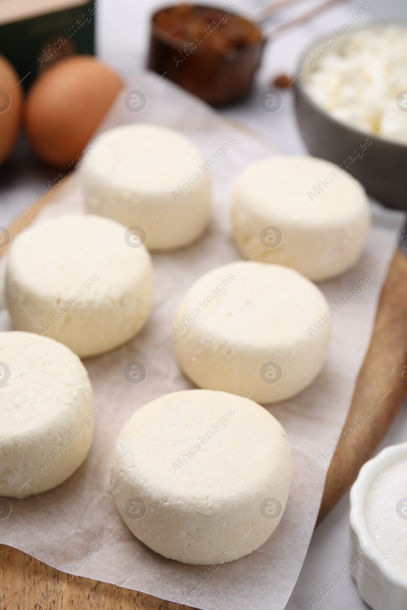 Photo of Uncooked cottage cheese pancakes and different ingredients on white table