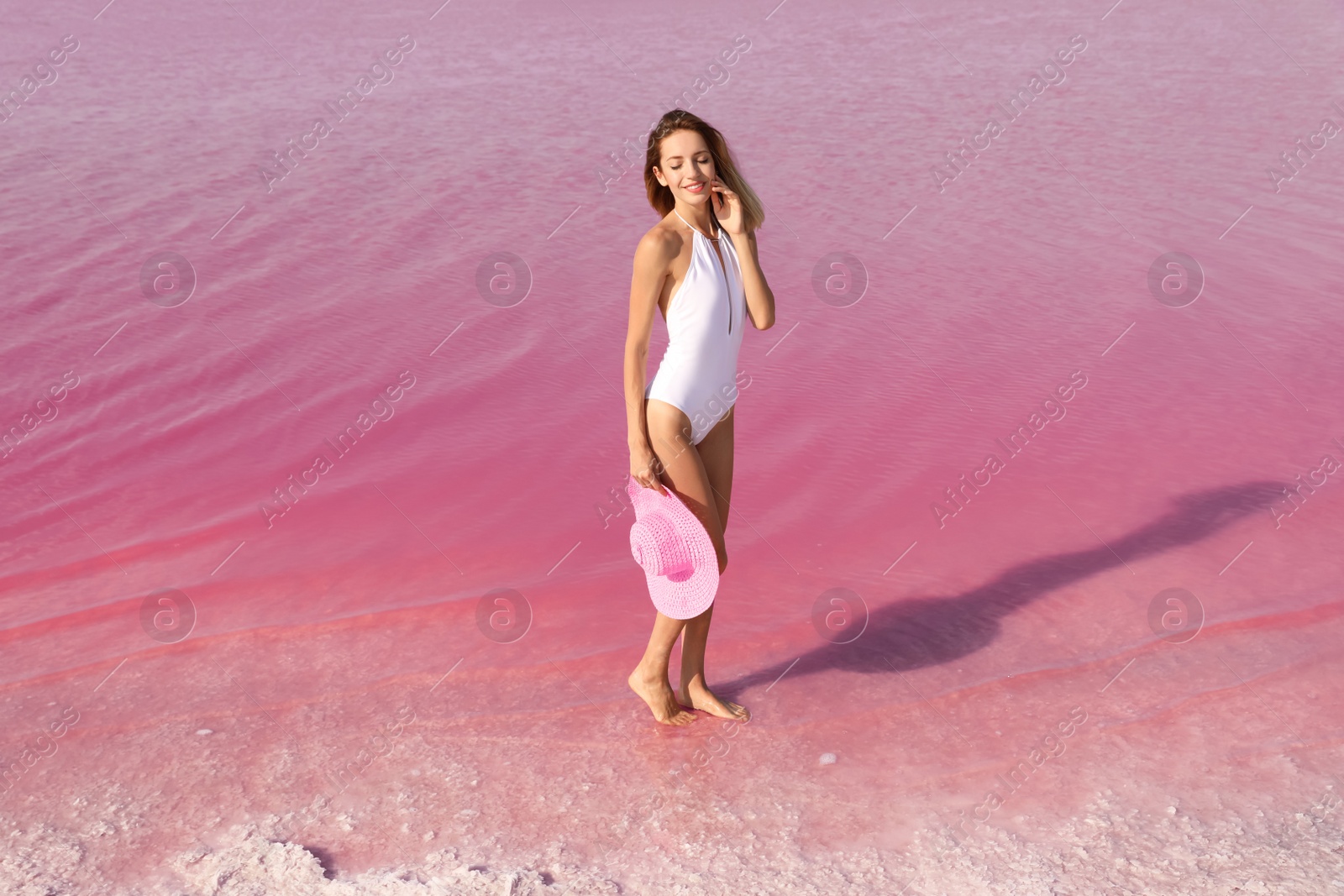 Photo of Beautiful woman in swimsuit posing near pink lake on sunny day