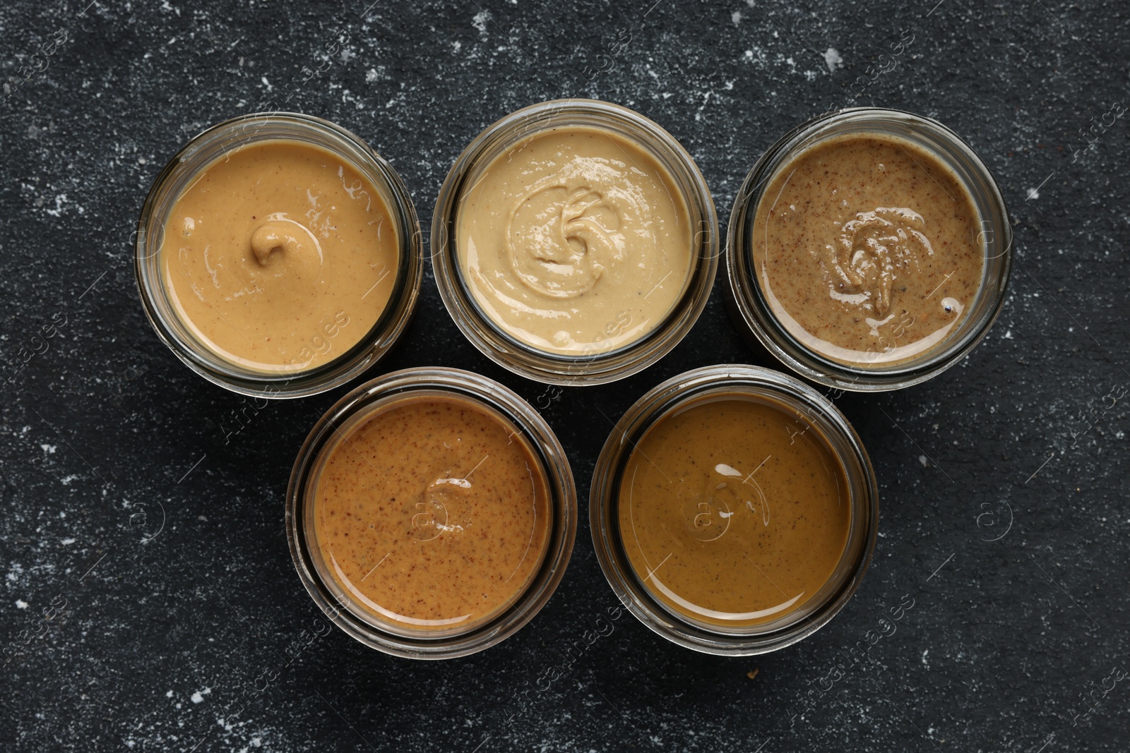 Photo of Tasty nut butters in jars on dark gray table, flat lay