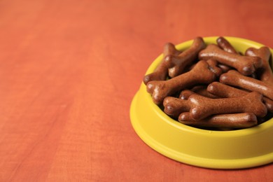 Photo of Yellow bowl with bone shaped dog cookies on wooden table, closeup. Space for text