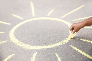 Little child drawing sun with chalk on asphalt