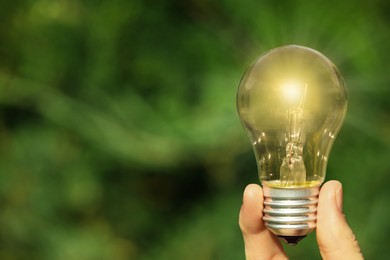 Image of Woman holding glowing light bulb outdoors, closeup. Space for text