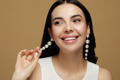 Photo of Young woman wearing elegant pearl earrings on brown background