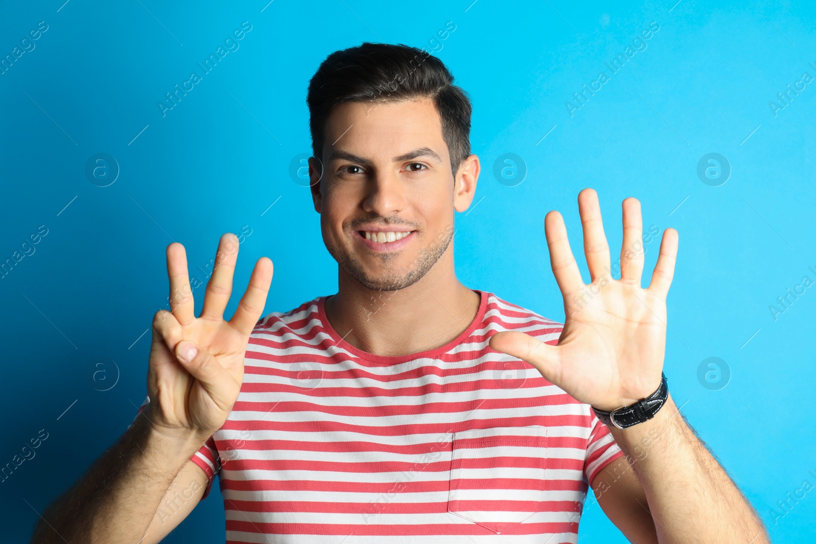 Photo of Man showing number eight with his hands on light blue background