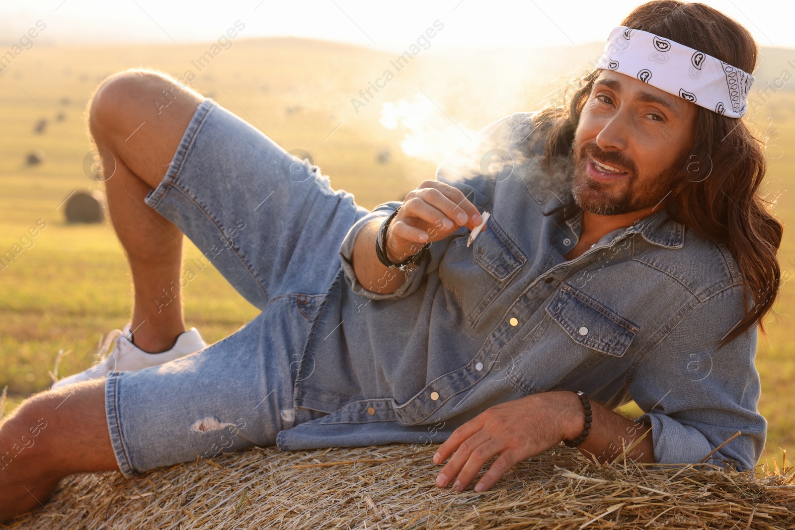 Photo of Hippie man smoking joint on hay bale in field