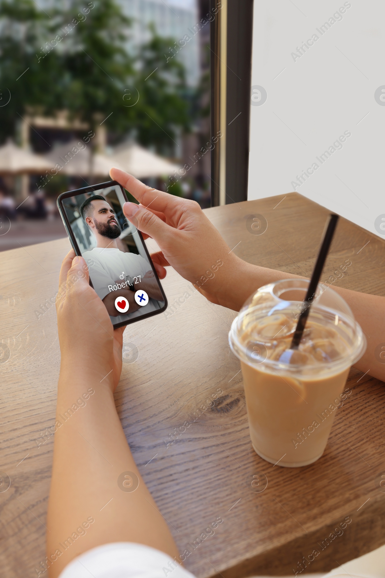 Image of Woman viewing male profile on dating site via mobile phone at cafe, closeup