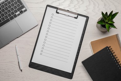 Clipboard with checkboxes, pen and laptop on wooden table, flat lay