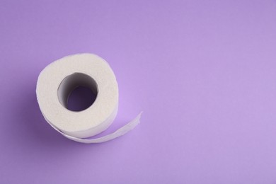 Photo of Soft toilet paper roll on violet background, top view. Space for text