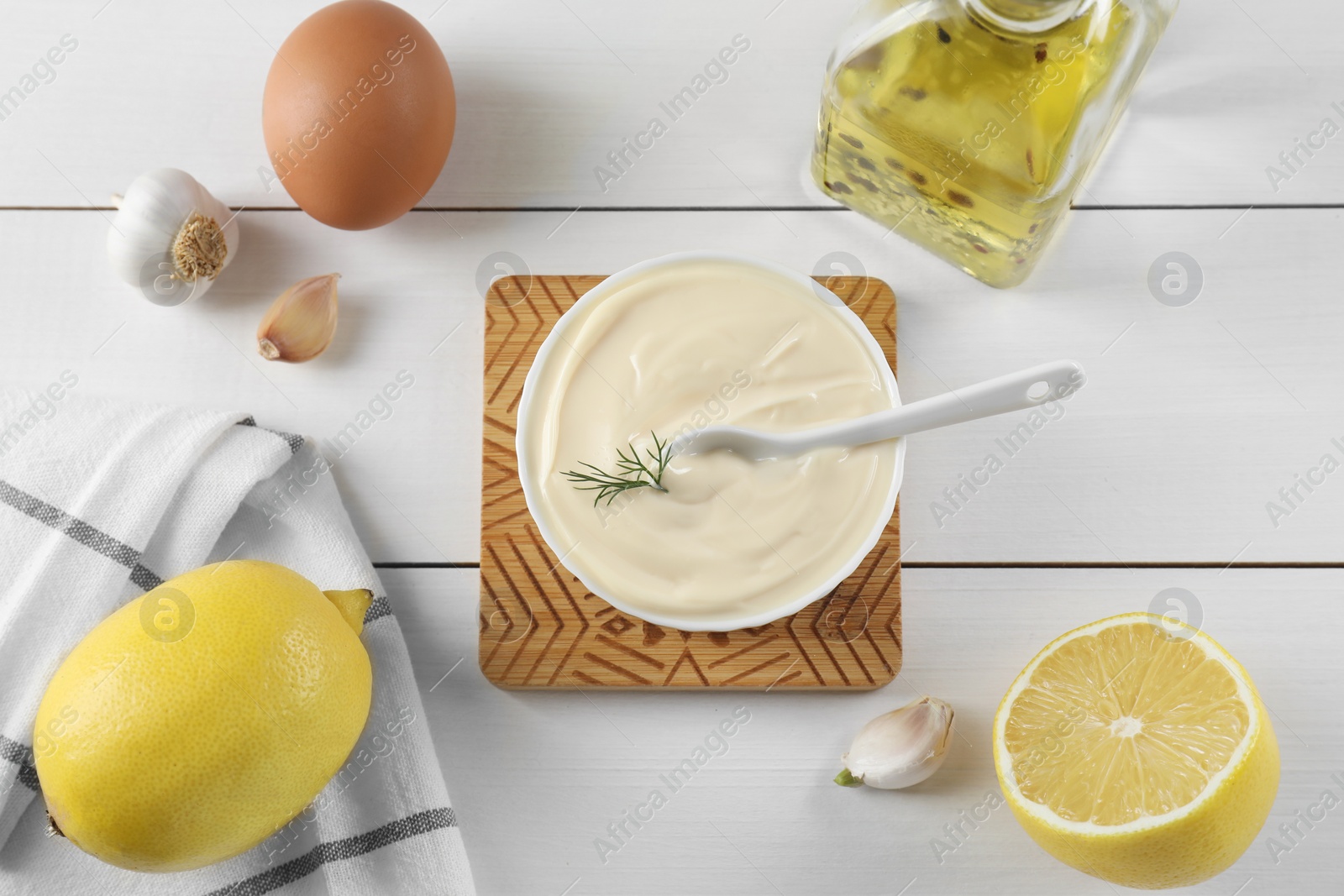 Photo of Fresh mayonnaise sauce in bowl and ingredients on white wooden table, flat lay