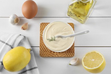 Photo of Fresh mayonnaise sauce in bowl and ingredients on white wooden table, flat lay