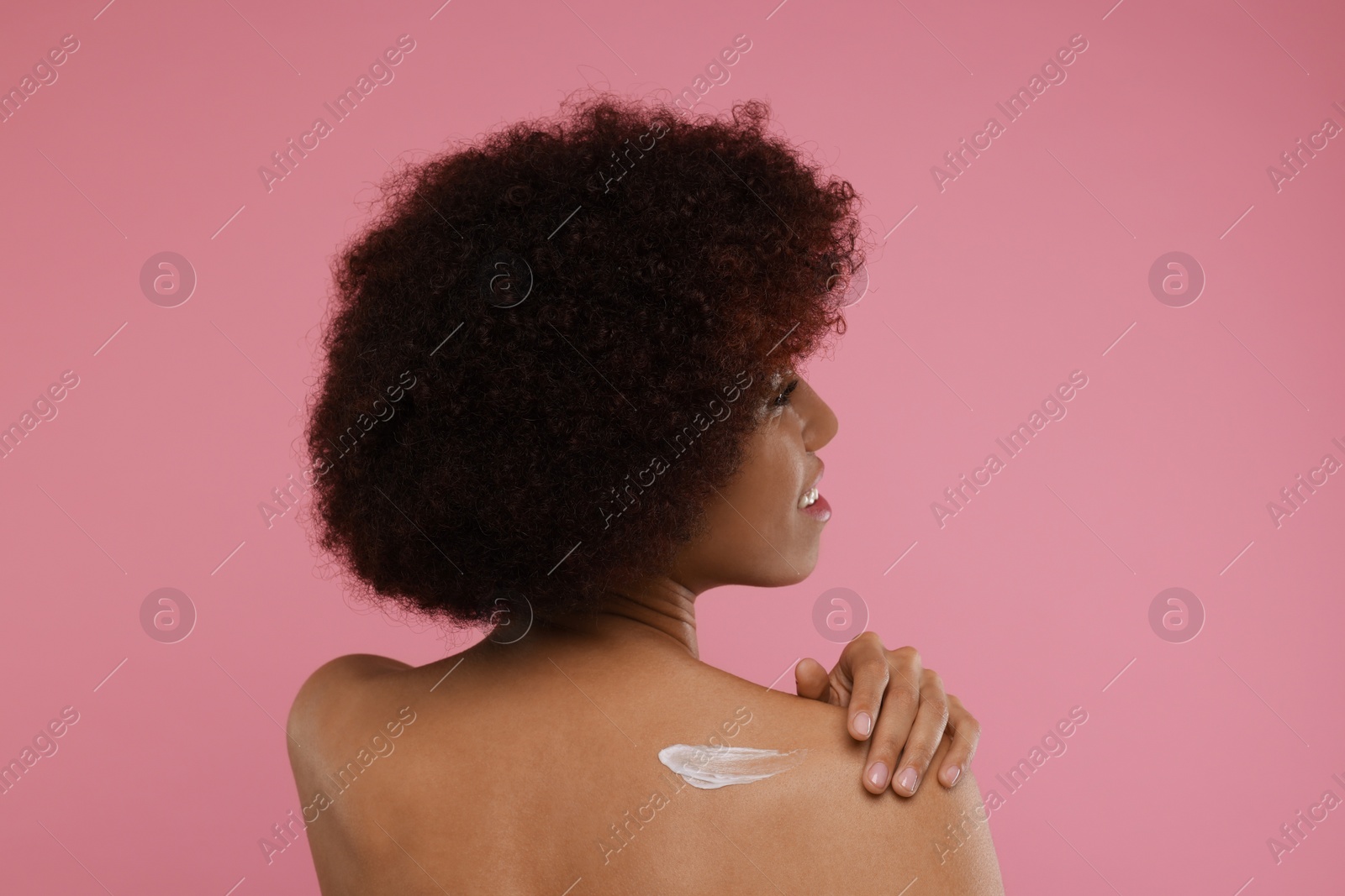 Photo of Beautiful young woman applying body cream onto back on pink background