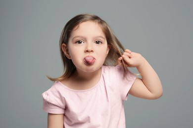Photo of Funny little girl showing her tongue on grey background