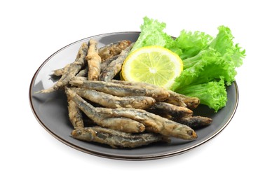 Plate with delicious fried anchovies, lemon and lettuce leaves on white background
