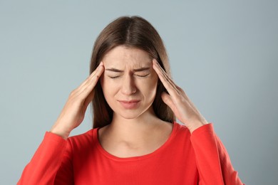 Young woman suffering from migraine on grey background