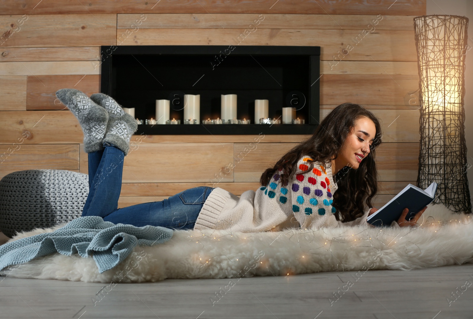 Photo of Young beautiful woman in warm sweater reading book on rug at home