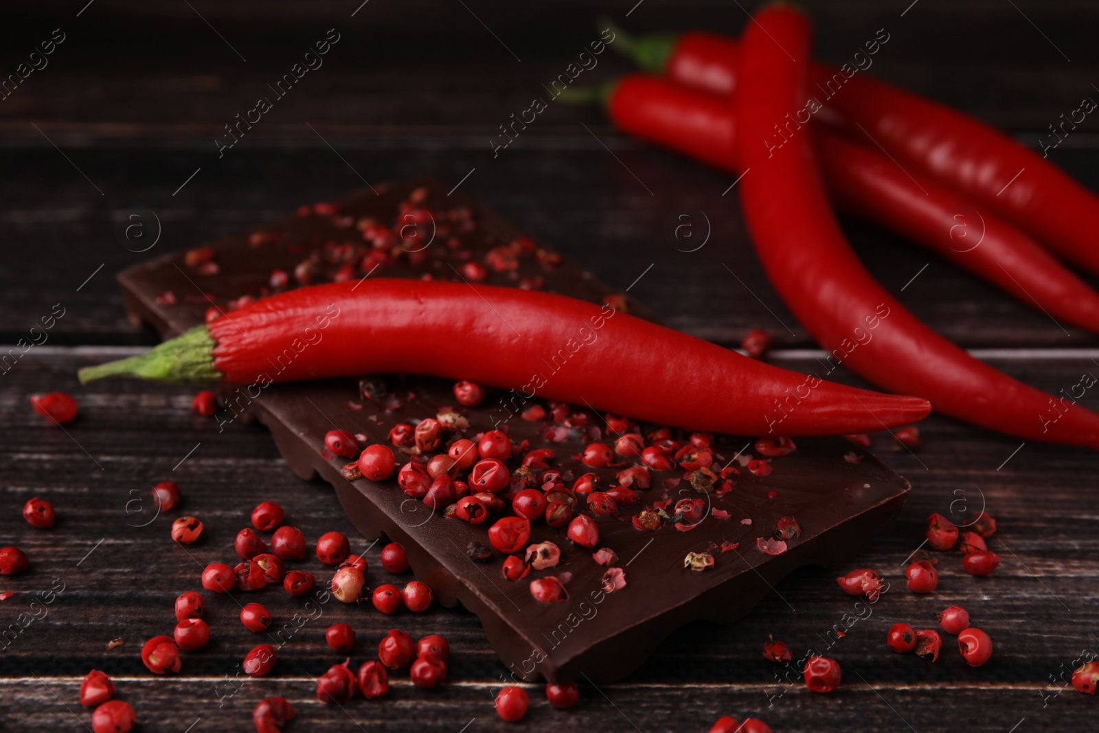 Photo of Delicious chocolate, fresh chili pepper and red peppercorns on wooden table, closeup