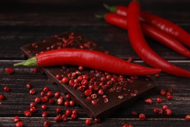 Photo of Delicious chocolate, fresh chili pepper and red peppercorns on wooden table, closeup