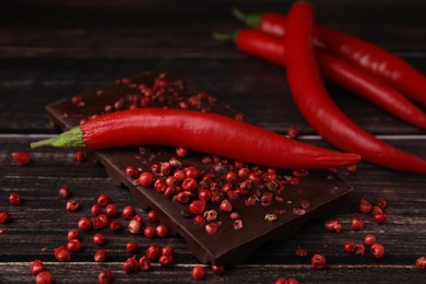 Delicious chocolate, fresh chili pepper and red peppercorns on wooden table, closeup