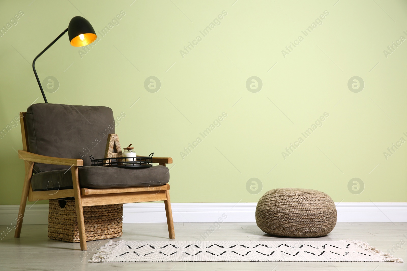 Photo of Stylish room interior with comfortable knitted pouf and armchair near light green wall