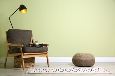 Stylish room interior with comfortable knitted pouf and armchair near light green wall