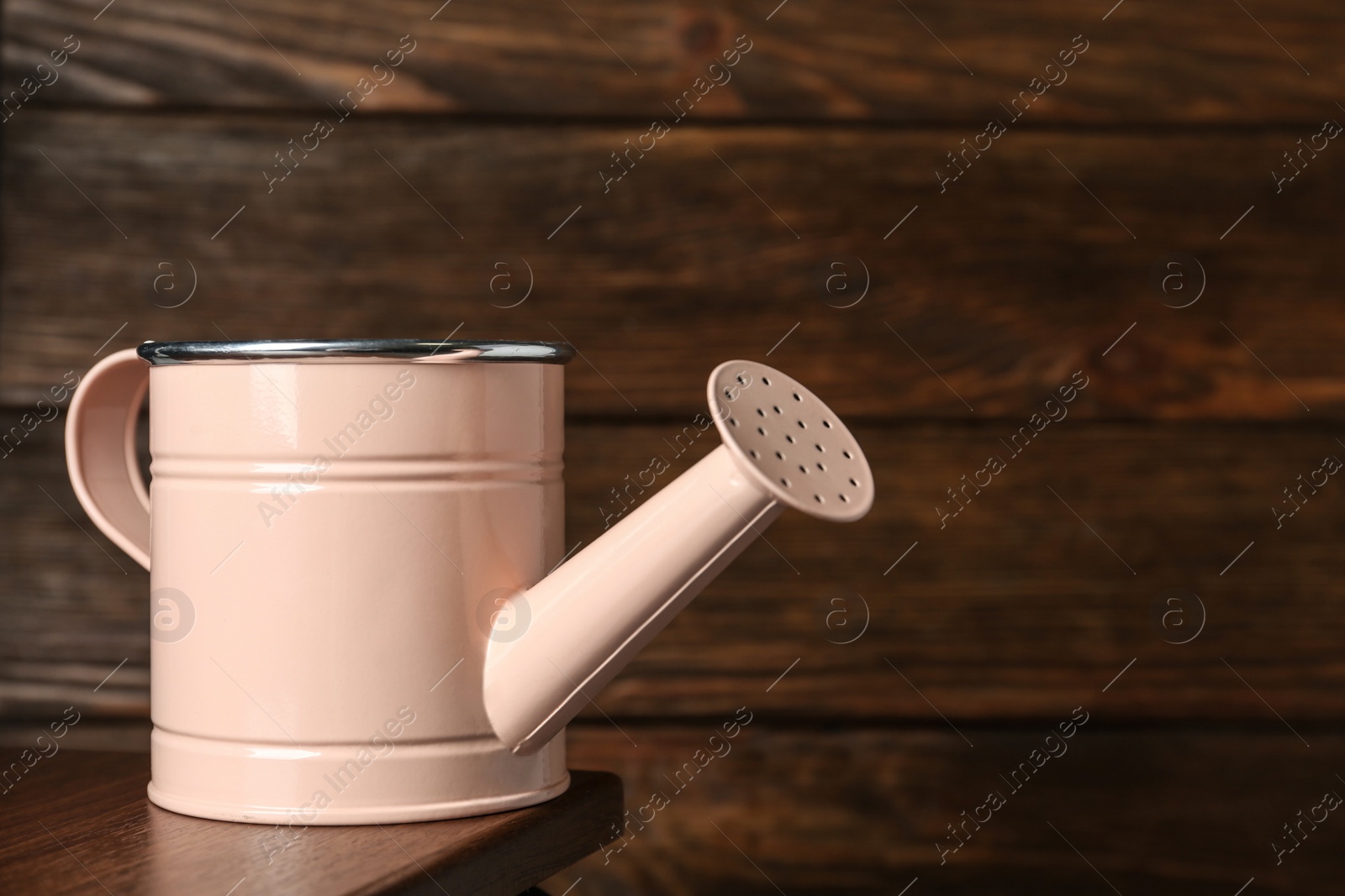 Photo of Pink metal watering can on table against wooden background