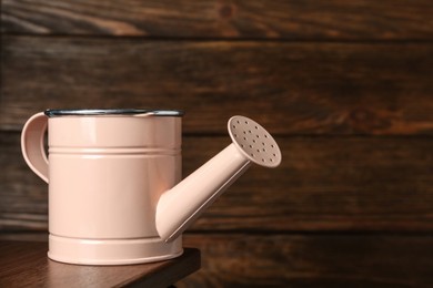 Pink metal watering can on table against wooden background