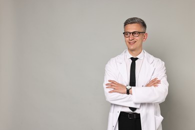 Happy doctor in glasses on grey background, space for text